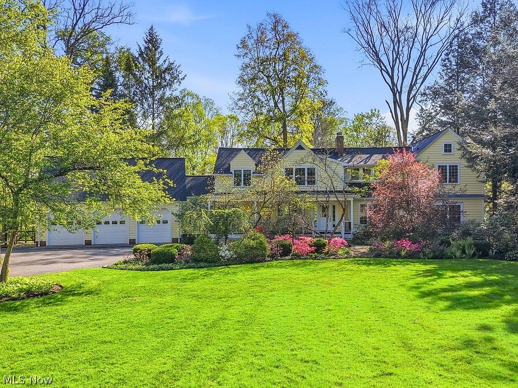 Front elevation of the yellow 1936 Colonial framed by mature trees and spring lawn