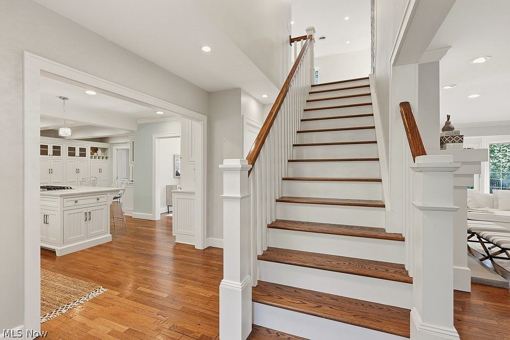 Interior entry with white wainscoting, oak staircase with stained treads, and a glimpse into the white kitchen with hardwood floors