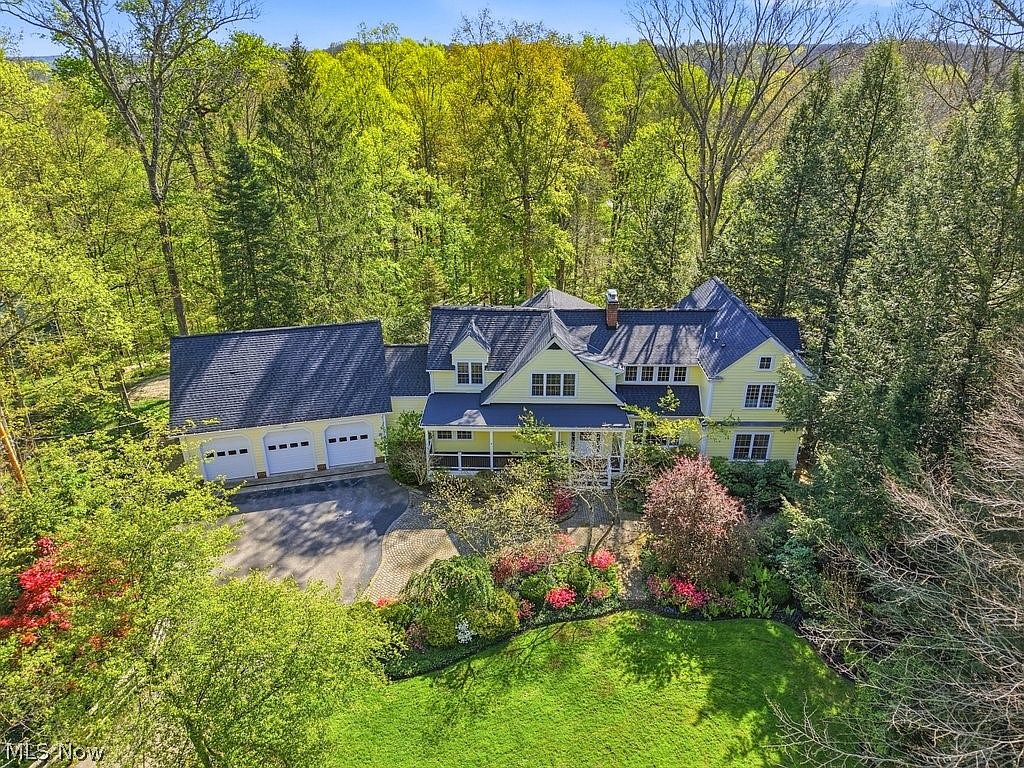 Aerial overview of the property showing the colonial, attached garage, gravel drive, and 1.3 acres of mature trees in spring color